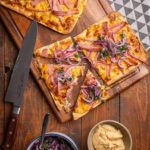 Leberkäs-Flammkuchen mit Obazda und frischem Zwiebelsalat auf einem Holzbrett