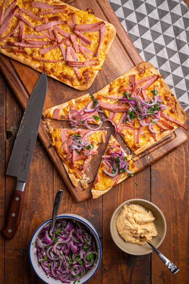 Leberkäs-Flammkuchen mit Obazda und frischem Zwiebelsalat auf einem Holzbrett