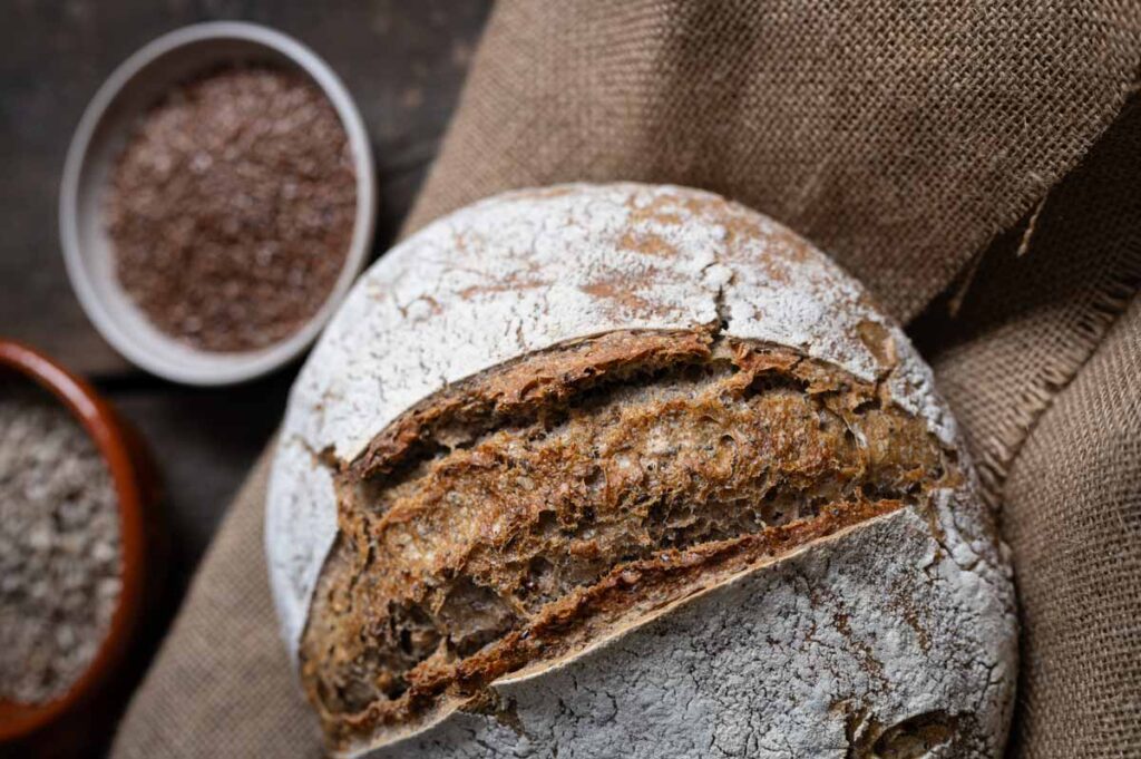 Rundes Körner-Sauerteigbrot mit Dinkelmehl und Saaten auf einem Holzbrett